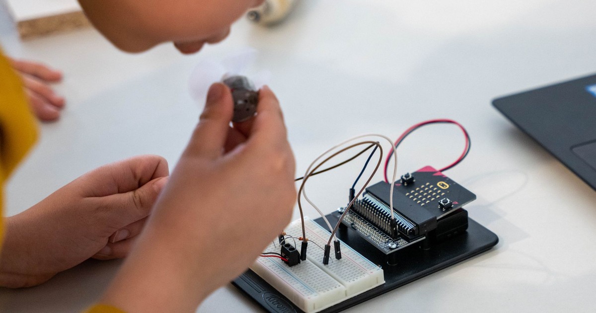 Young child assembling an electronic circuit with a microcontroller on a workbench.