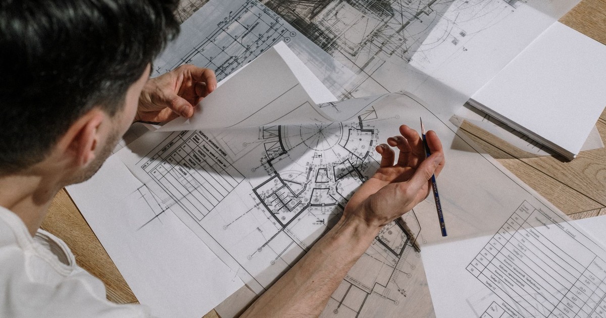 Architect studying and sketching over detailed architectural blueprints indoors.
