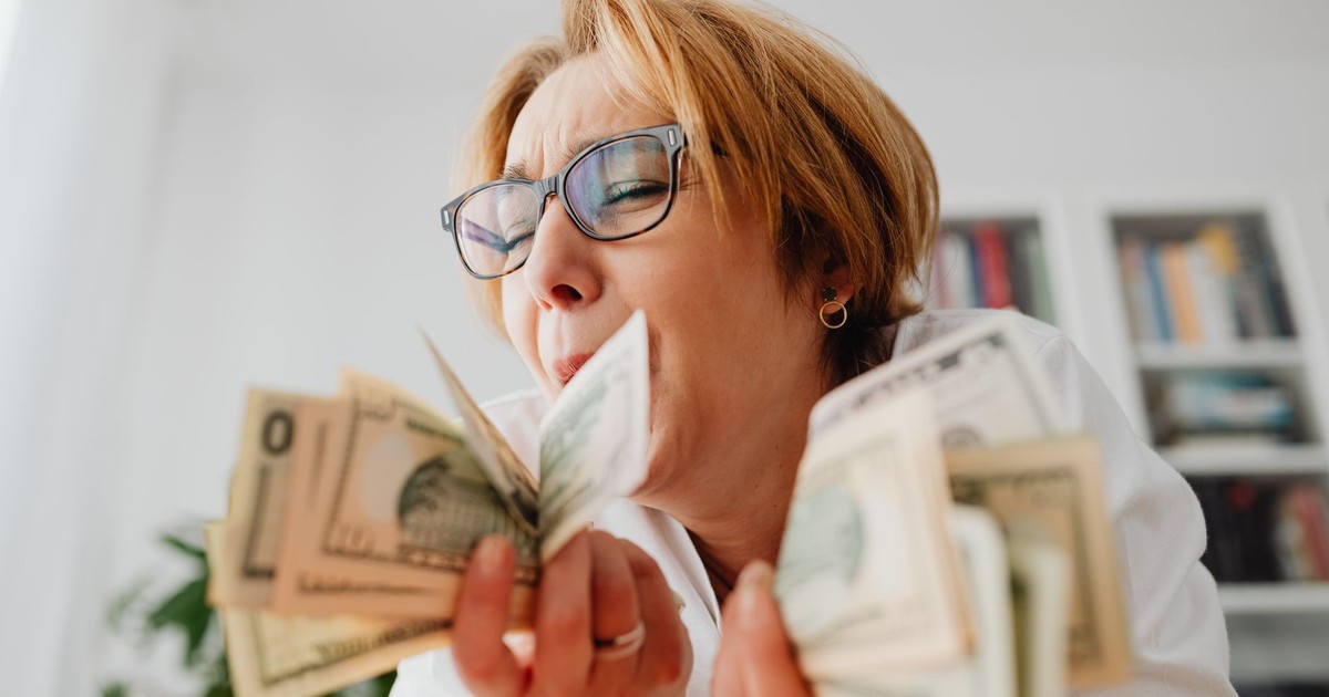 A happy woman with eyeglasses cherishing US dollar bills indoors, symbolizing wealth and financial success.