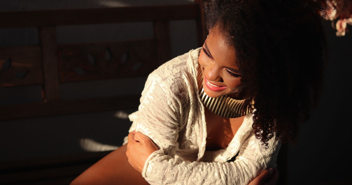 Elegant woman in a sunlit room with a joyful expression and stylish attire.