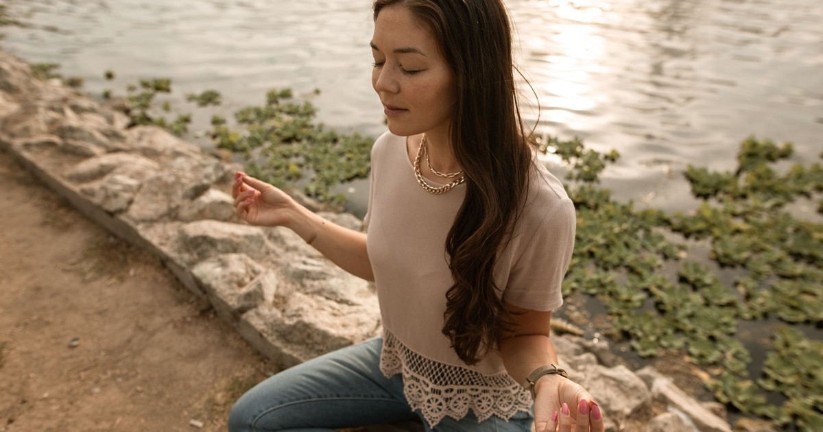 Woman meditating by a lake at sunset, embodying serenity and relaxation.