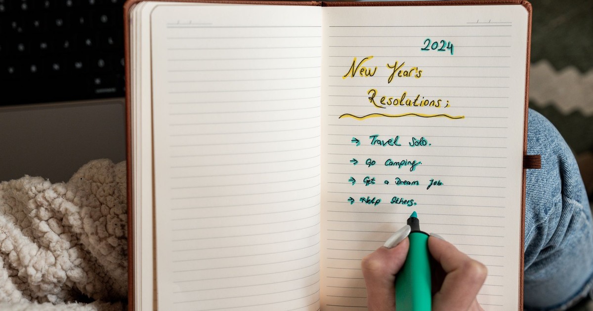 Person making 2024 New Year's resolutions in a notebook with a green marker.