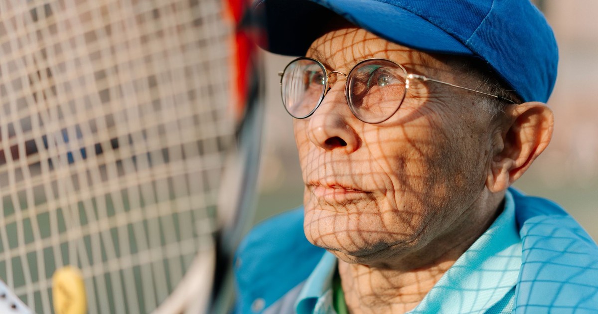 A senior man in sportswear standing with a tennis racket outdoors, enjoying leisure time.