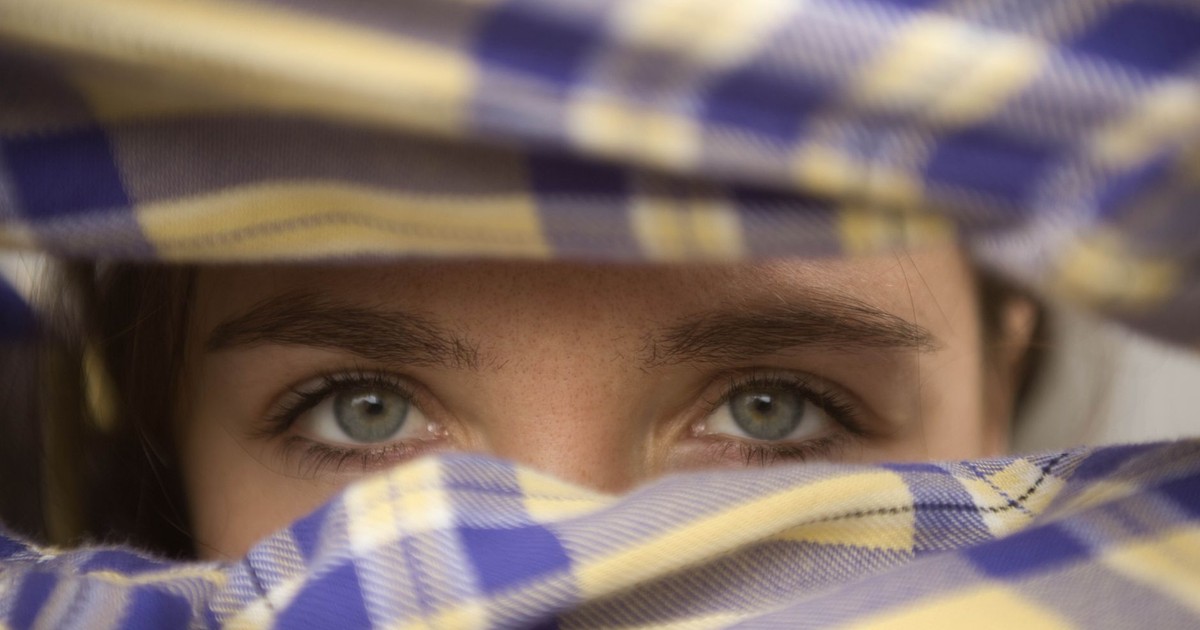 Artistic close-up portrait of woman's eyes peeking through plaid fabric.