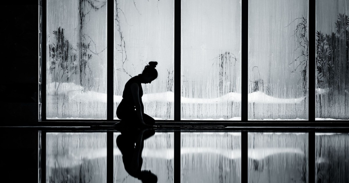 A woman kneels in meditation, silhouetted against a foggy window, reflecting tranquility.
