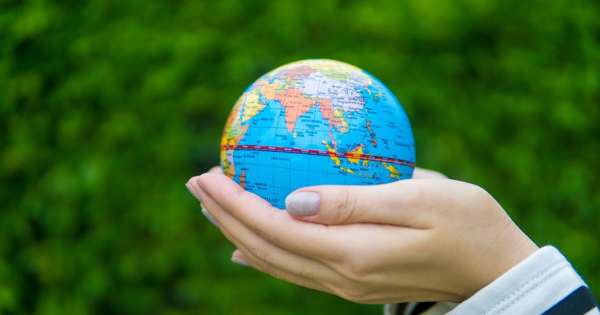 Close-up of hands gently cradling a miniature globe against a green backdrop.