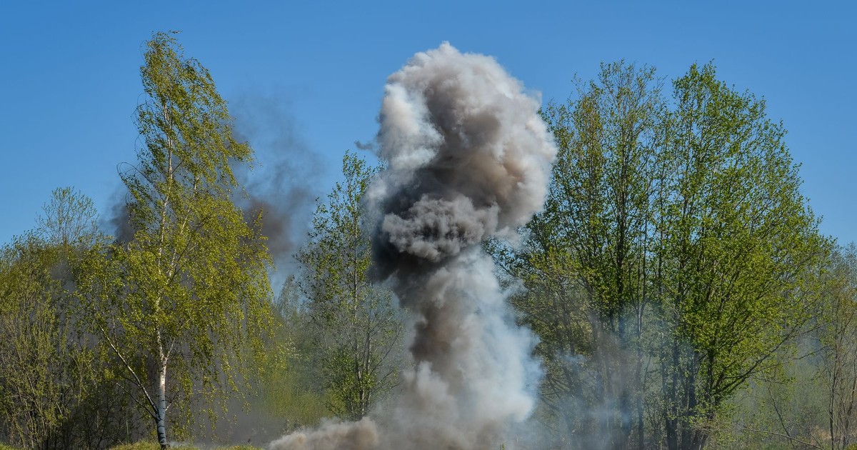 A powerful explosion creates a huge cloud of smoke against a backdrop of green trees, illustrating nature vs. destruction.