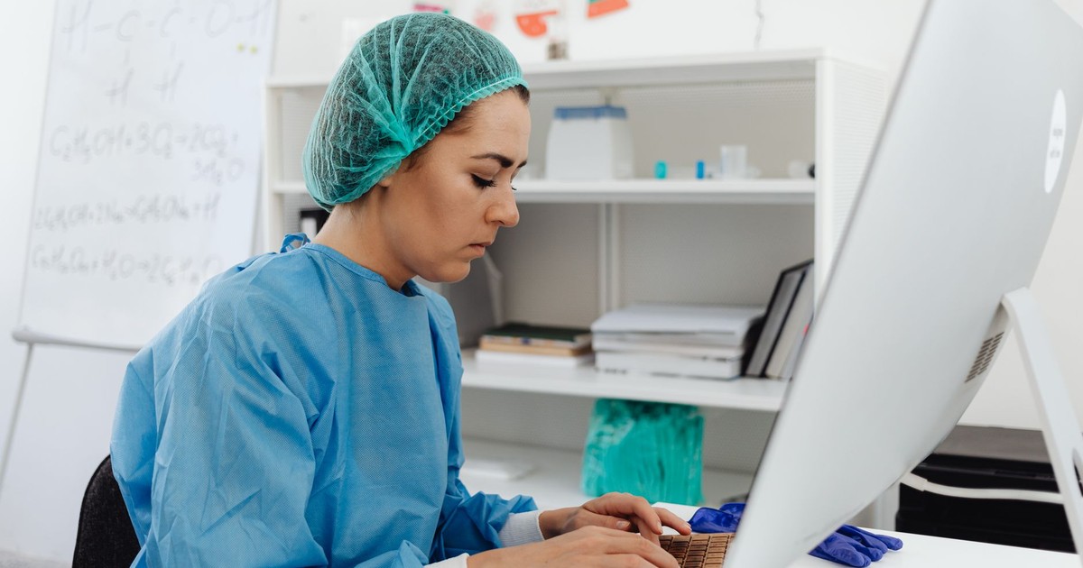A female healthcare professional in scrub suit working on a computer in a laboratory setting.