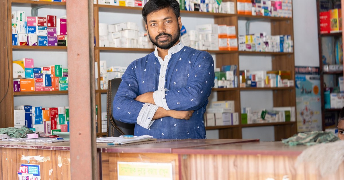 A confident pharmacist stands behind the counter of a pharmacy in Natore, Bangladesh.