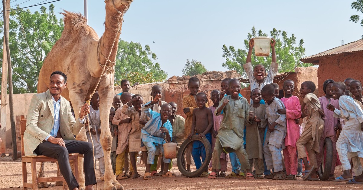 A cheerful gathering of people with a camel in an outdoor African village setting, full of life and happiness.