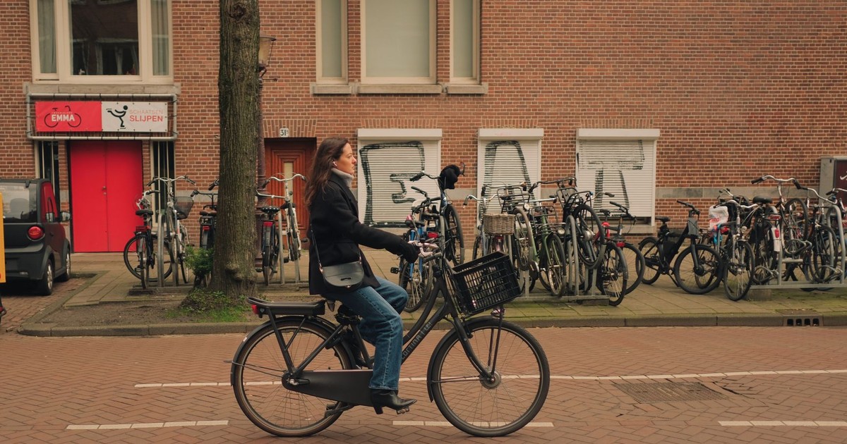 A woman rides a bicycle on a city street with many parked bikes around her.