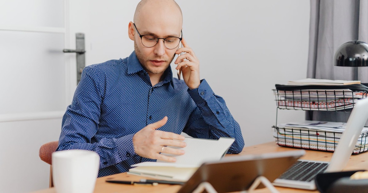 A bald professional man using a phone and making notes in an office environment.
