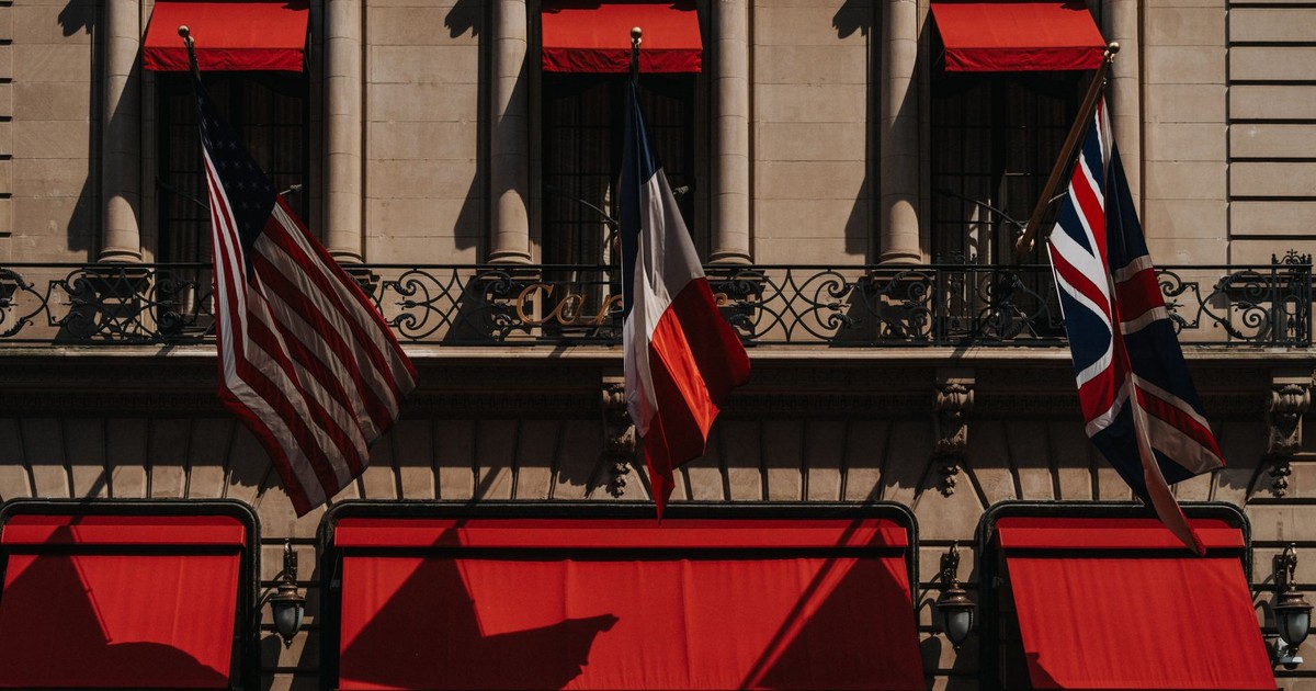 A classic building facade featuring US, French, and UK flags with vibrant red awnings.