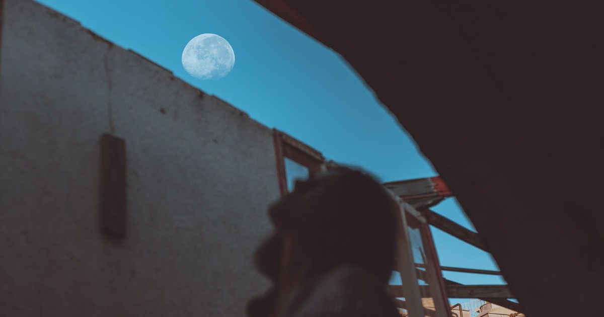 Low angle view of a silhouette person gazing at the moon through a building's opening.