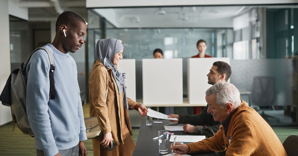 A diverse group of adults engaged in voting at an indoor polling station.