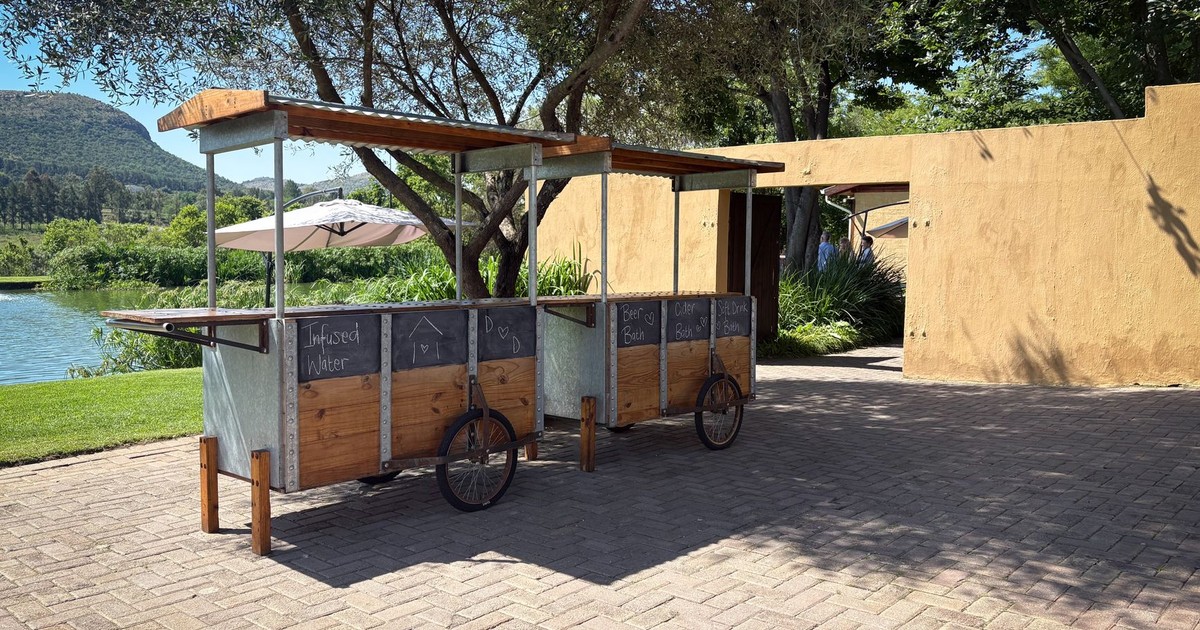 A rustic drink cart set outdoors by a river, offering beverages.