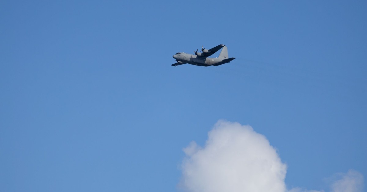 Lockheed C-130 Hercules aircraft flying against a clear blue sky with clouds.