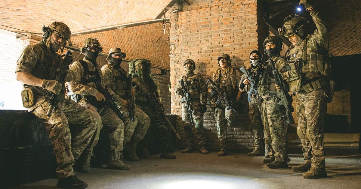 Soldiers in tactical gear gather in a brick underground tunnel with dim lighting.