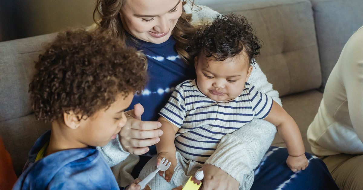High angle of African American boy playing with toys standing near smiling mother cuddling small baby