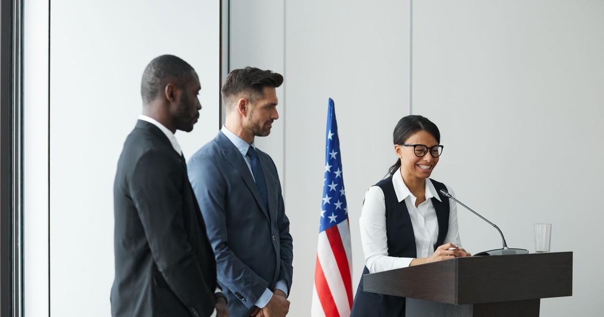 A diverse team in business attire at a podium with an American flag, showing unity and professionalism.