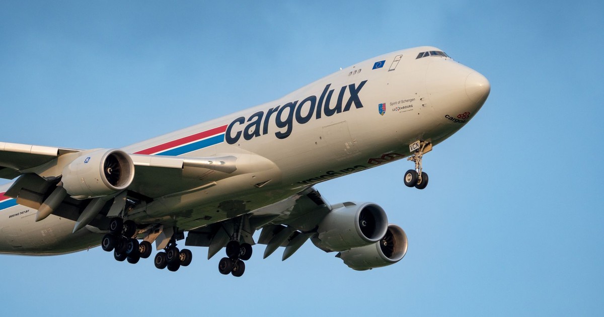 A Cargolux cargo plane flies against a clear blue sky, showcasing its massive structure.