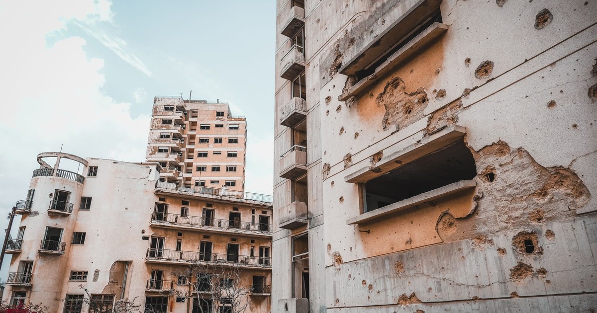 Damaged concrete buildings in Cyprus display signs of war and decay, under a blue sky.
