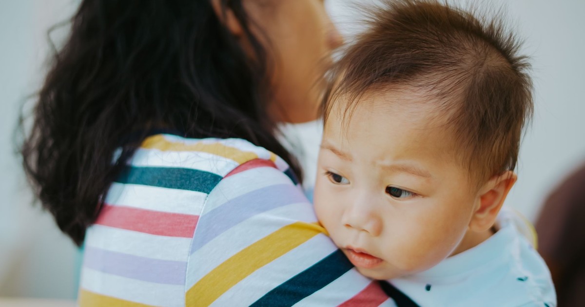 A woman lovingly holds an Asian baby boy indoors, showcasing a tender family moment.