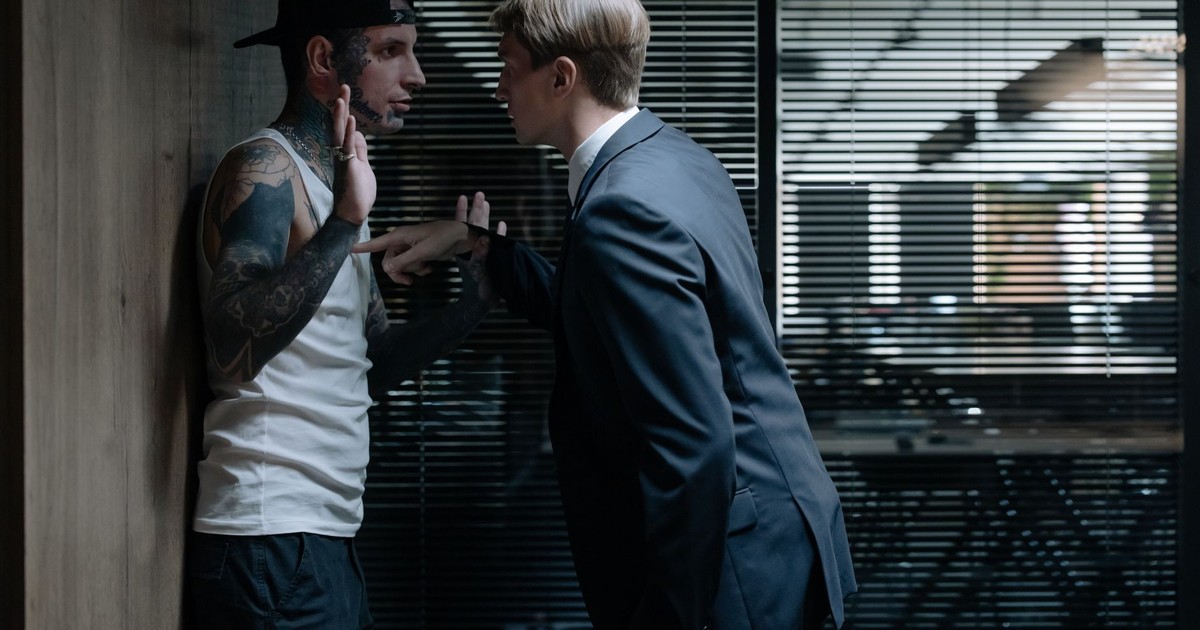 A businessman interrogating a tattooed suspect in an office environment, conveying tension.
