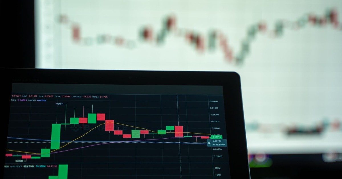 A laptop displays a detailed cryptocurrency trading chart with candlestick patterns.