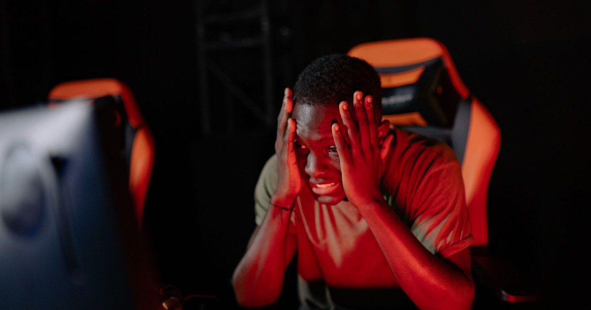 A man intensely reacts to a game loss at his computer in a dimly lit gaming room.