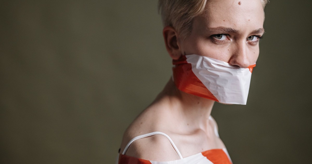 Artistic portrait of a woman with mouth covered by tape, symbolizing silence and oppression.
