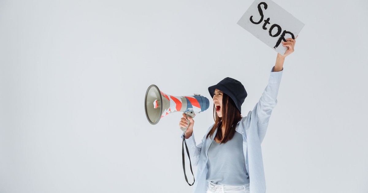 Woman passionately protesting with a megaphone and 'Stop' sign in a studio setting.