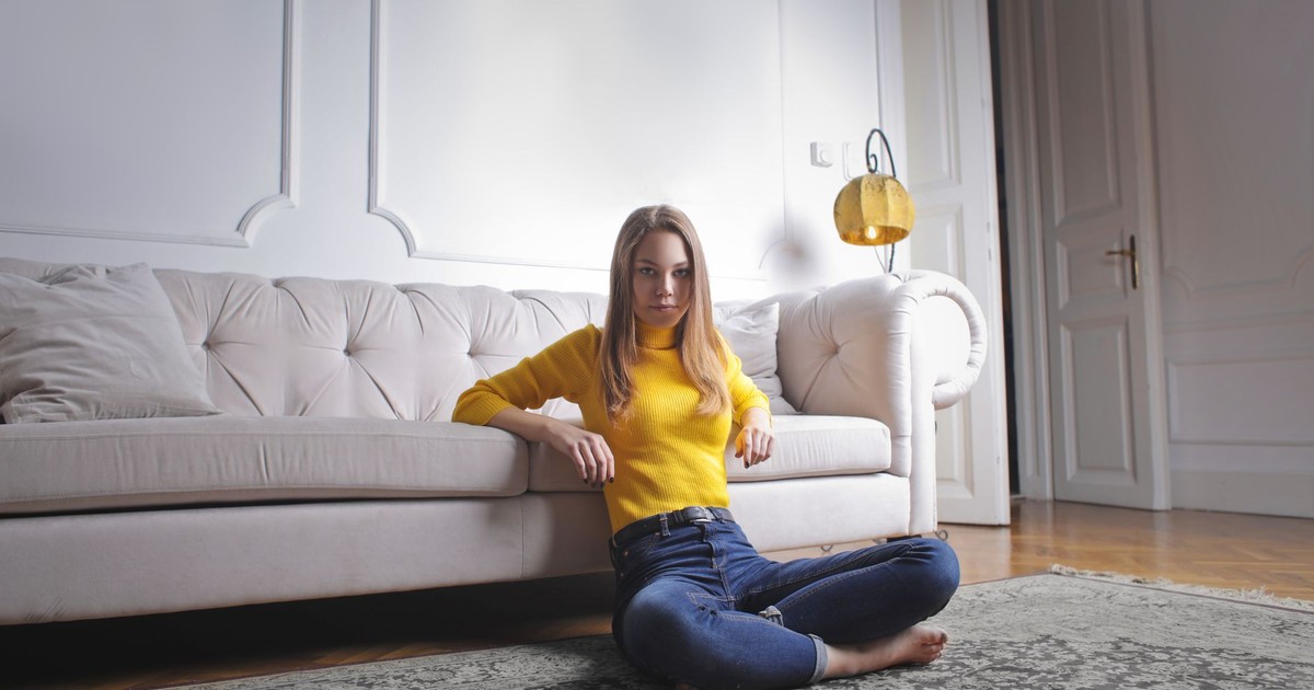 A young woman in a yellow sweater sitting on the floor in a stylish modern living room. Perfect for lifestyle themes.