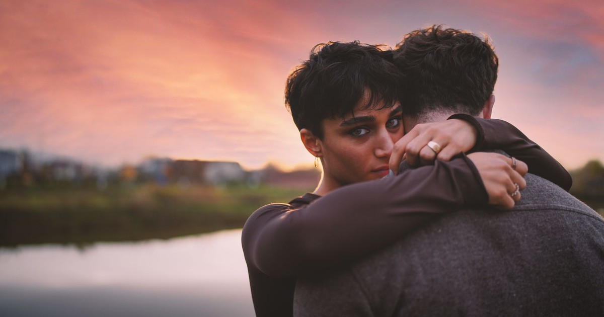 A couple embracing tenderly by the lake during a vibrant sunset, conveying love and warmth.