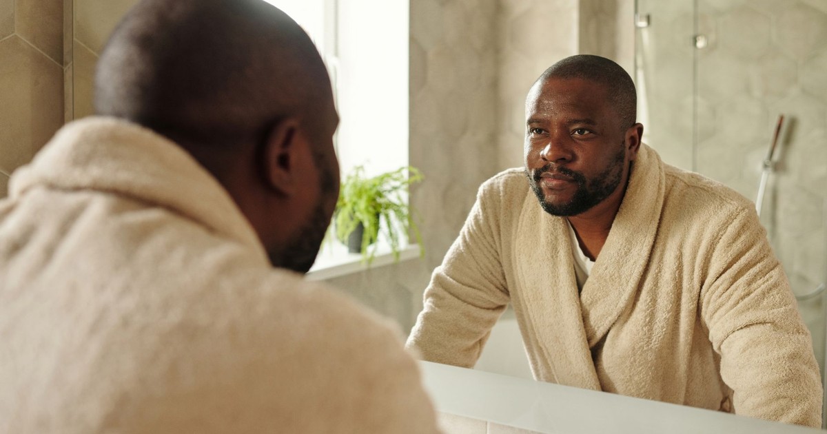 Adult man in a bathrobe looking at his reflection in a bathroom mirror. Morning routine concept.