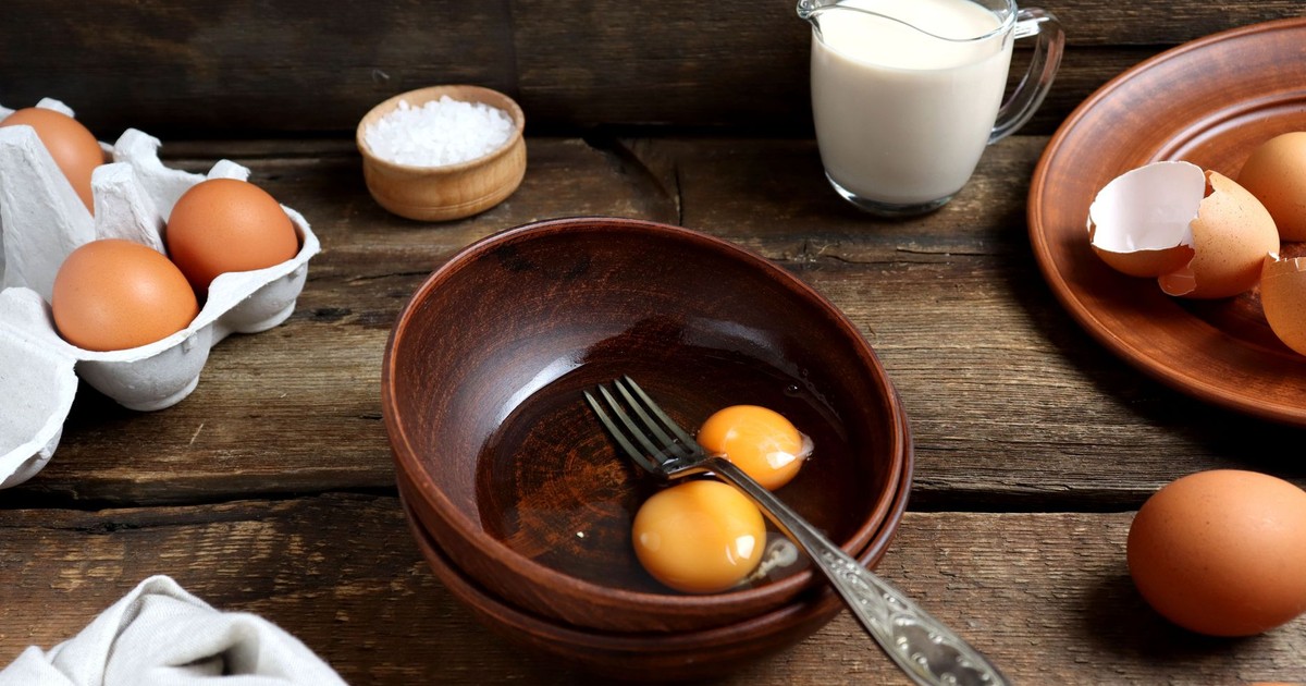 Still life photograph featuring eggs, milk, and kitchenware on a rustic wooden table.