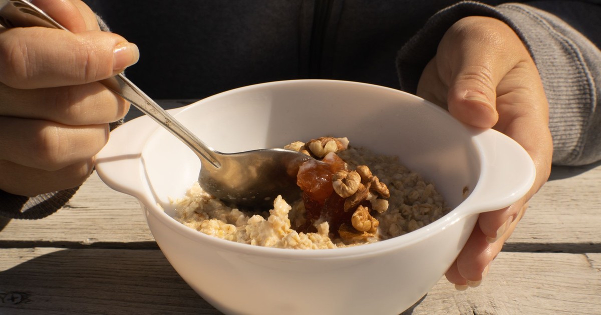 A bowl of oatmeal topped with walnuts and honey held by a person. Perfect nutritious breakfast option.