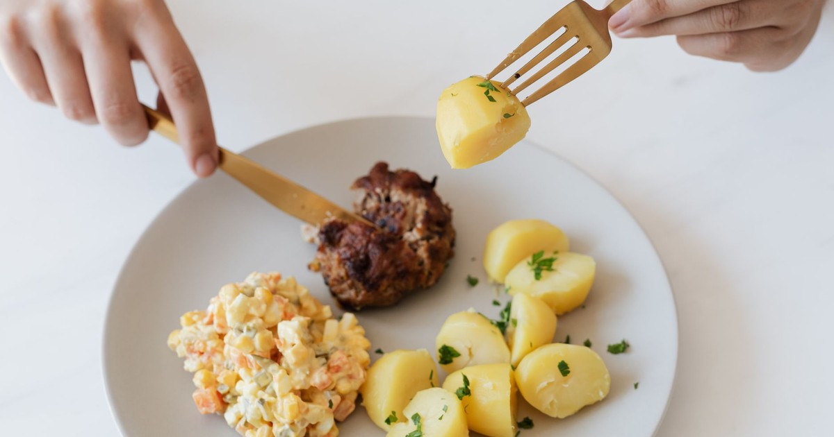 From above of crop anonymous person with cutleries eating delicious fried cutlet and hot boiled potatoes with parsley garnished with nutritious Russian salad
