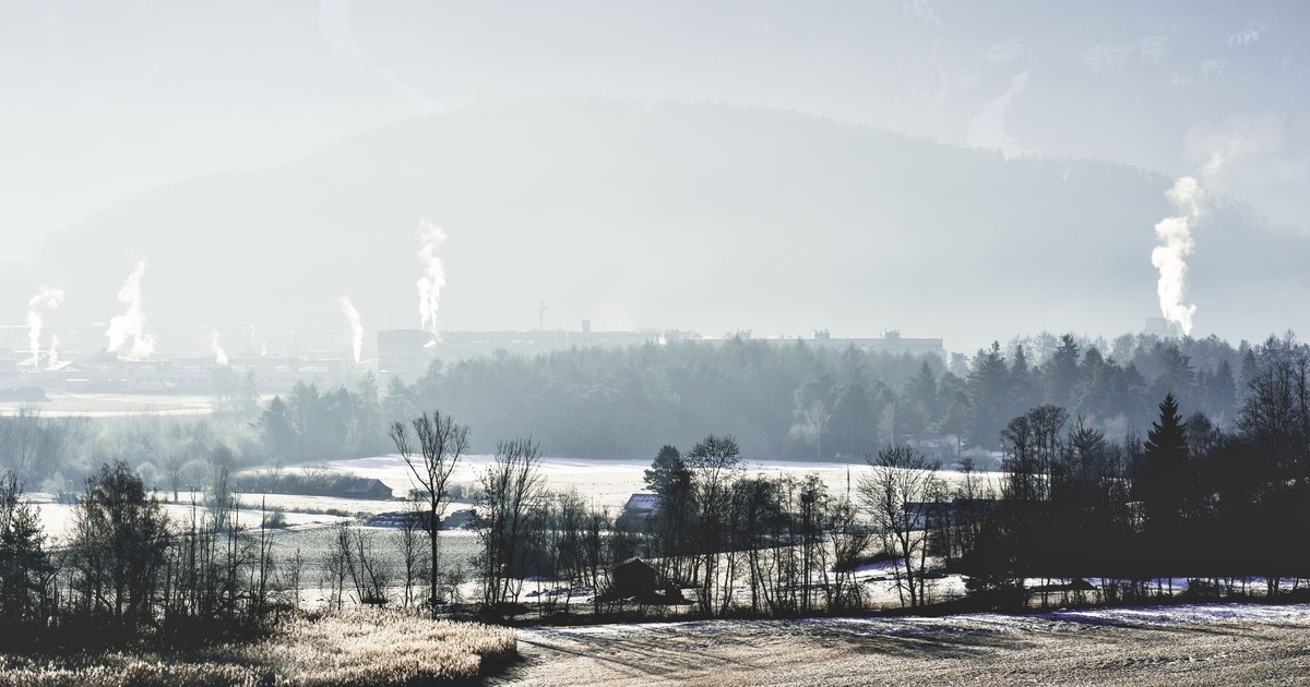 A tranquil winter scene featuring snow-covered fields and distant industrial factories emitting smoke.