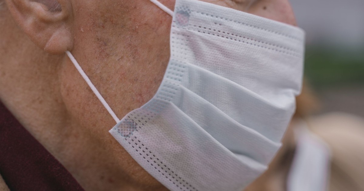 Detailed shot of an elderly man wearing a protective face mask, highlighting facial details and mask texture.