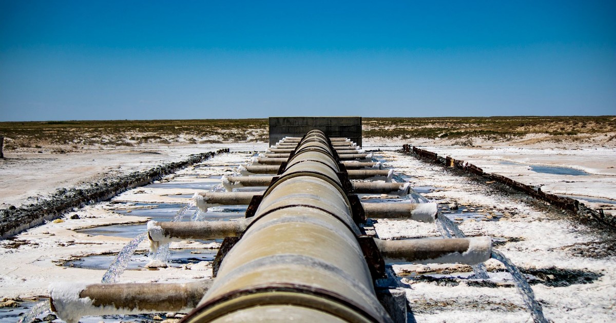 Large industrial pipeline discharging wastewater in arid, rural landscape under clear blue sky.
