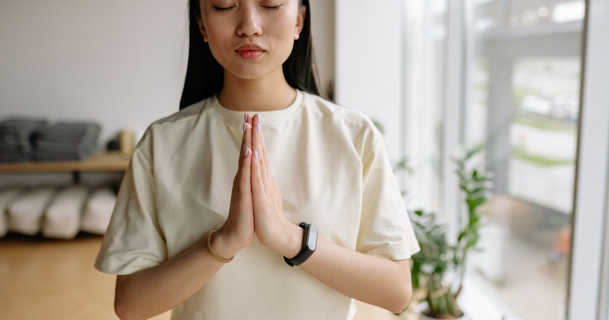 Young woman practicing meditation indoors, symbolizing peace and relaxation with eyes closed.