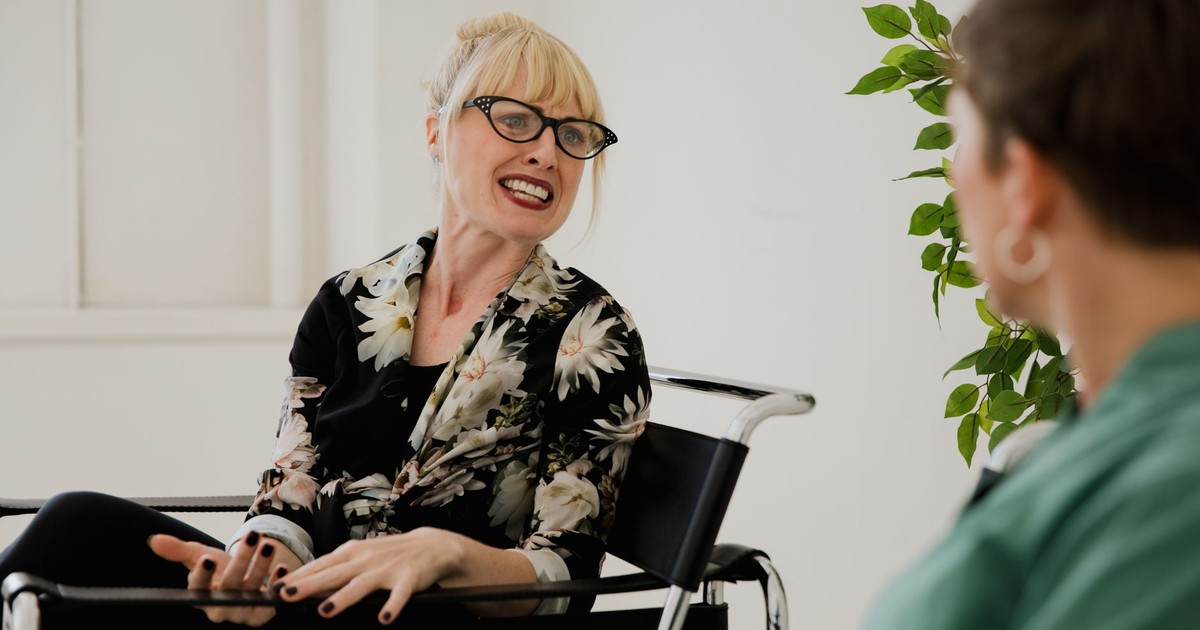 Blonde woman with glasses actively talking during an indoor counseling session.