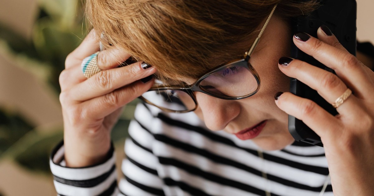 Crop upset adult female manager in eyeglasses feeling sad while having phone discussion during work in office