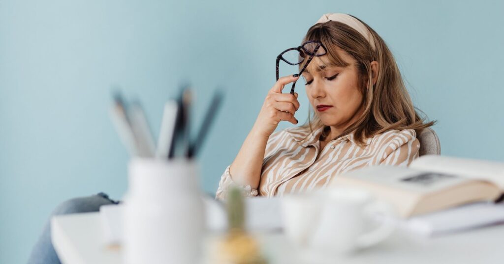 Caucasian woman looks exhausted while taking a break with eyes closed at her desk.