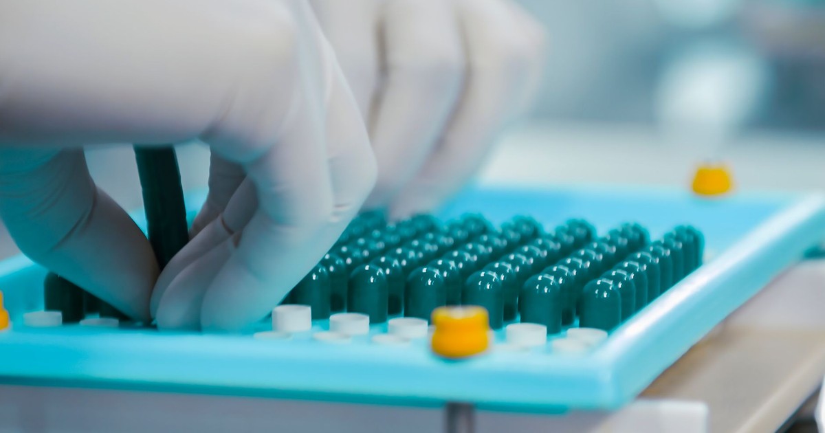 Close-up of gloved hands working with capsules in a pharmaceutical lab setting.