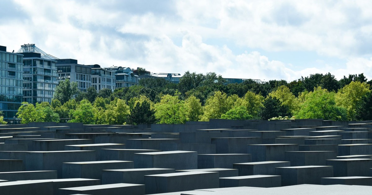 View of the Holocaust Memorial in Berlin with a backdrop of trees and a cloudy sky.