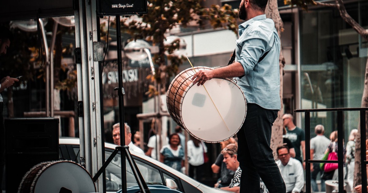Man in urban setting plays a traditional drum during a lively street performance.