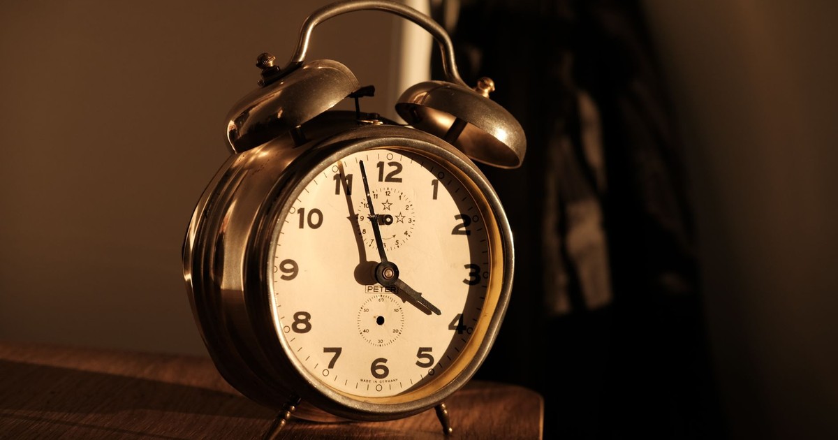 Old-fashioned alarm clock on wooden surface with warm lighting.