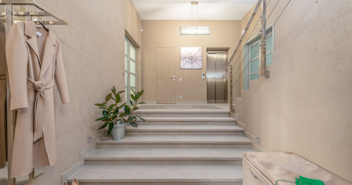 Modern lobby with elevator and wide staircase leading to hallway with bench and hanger shelf